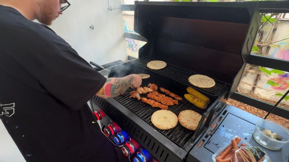 Someone grilling chicken skewers, corn and pita