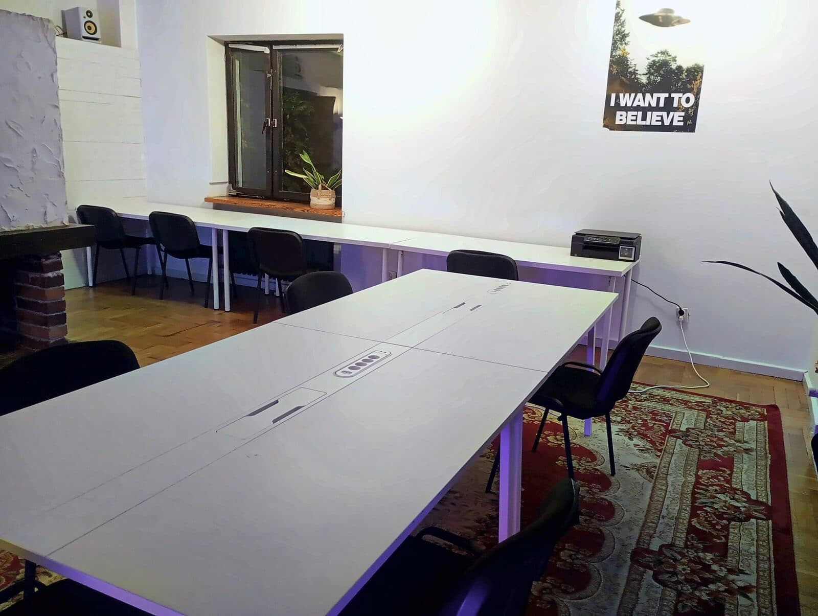 The coworking room: a long shared table with power strips, and a row of desks under the window