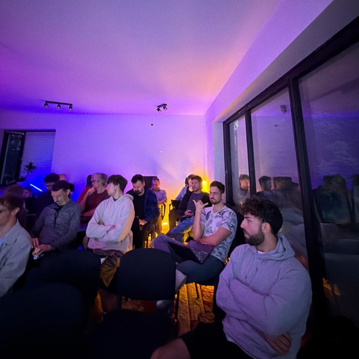 Workshop attendees seated in a room lit purple, listening to the speaker